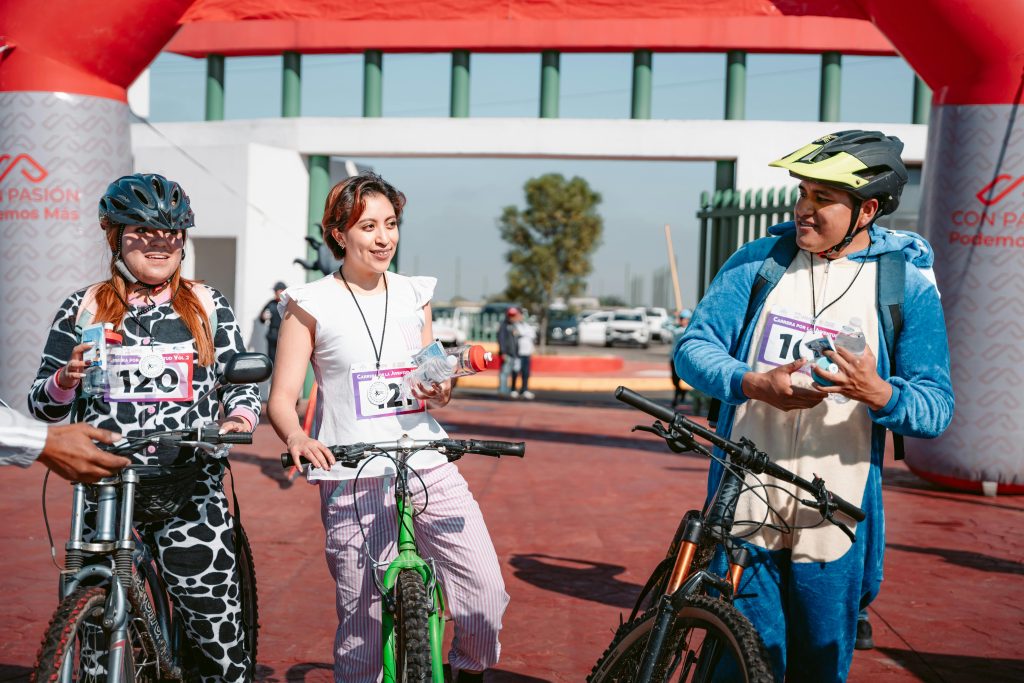 Three cyclists in costume celebrate the end of a race by the finish line arch outdoors.